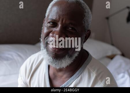 Portait von Senior african american Mann auf dem Bett sitzend Blick auf Kamera und lächelnd. Zu Hause in Selbstisolation während Quarantäne-Sperre bleiben. Stockfoto