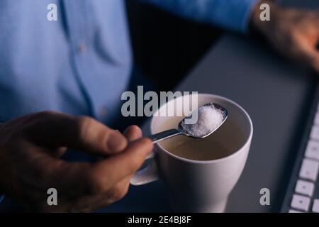 Nahaufnahme der Hände unkenntlich Mann Gießen Zucker auf Kaffee In Tasse mit kleinem Metalllöffel Stockfoto