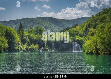 Türkisfarbener See und Wasserfälle von Sonnenlicht mit Wald bedeckt grünen Hügeln beleuchtet, Plitvicer Seen Nationalpark UNESCO-Weltkulturerbe, Kroatien Stockfoto