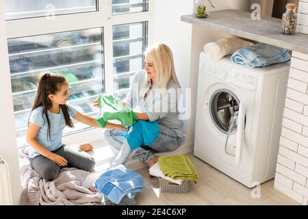 Familie Mutter und Kind Mädchen kleinen Helfer in Waschküche In der Nähe von Waschmaschine und schmutzige Kleidung Stockfoto