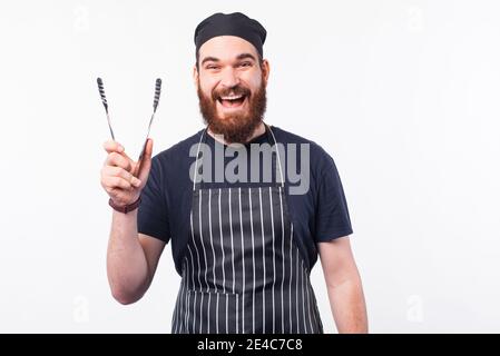 Foto des glücklichen Chefkochs Mann hält Utensil zum Kochen Fleisch. Stockfoto