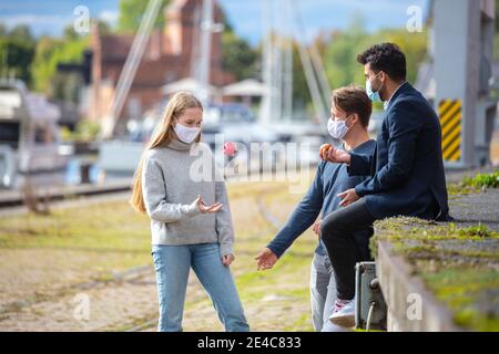 Zwei Männer und eine Frau in Corona-Zeit, mit Alltagsmasken, in der Stadt. Freizeit mit Maske im Freien. Stockfoto