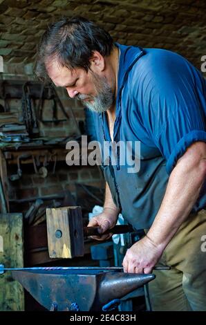 Der Schmied Ralph Oalmann formt in seinem Geschäft in Fort Gaines, 5. August 2017, auf Dauphin Island, Alabama, mit einem Holzhammer ein Stück Metall. Stockfoto