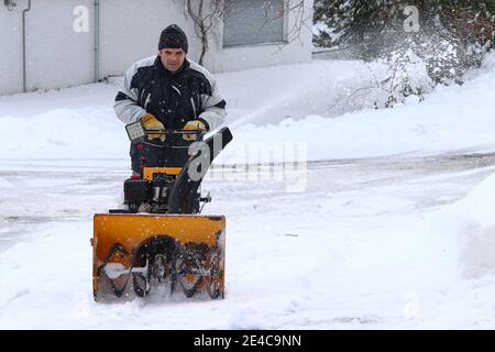 Ein Mann räumt die Straße und den Bürgersteig mit einem Schneegebläse Stockfoto