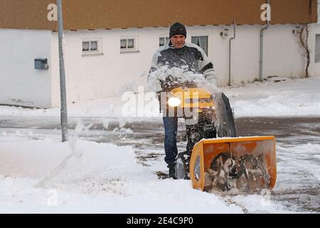 Ein Mann räumt die Straße und den Bürgersteig mit einem Schneegebläse Stockfoto