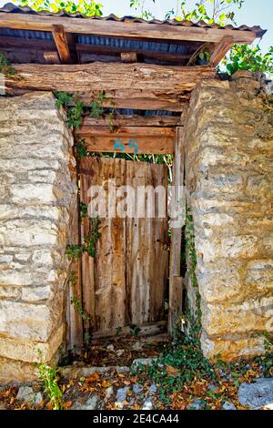 Verwitterte Holztür zwischen mächtigen Mauern in Monodendri, Zagori Dörfern, Pindus Bergen, Epirus, Nordgriechenland Stockfoto