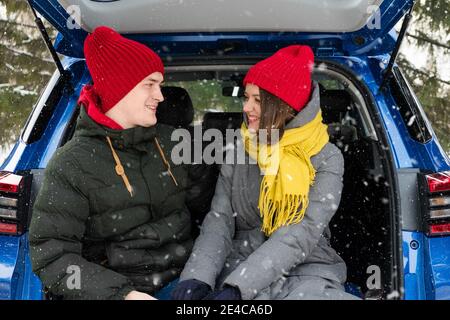 Romantisches junges Hipster-Paar umarmt, während im Kofferraum unter fallendem Schnee sitzt. Liebe, Valentinstag und Urlaubskonzept. Kuss und Umarmung. Valentinstag Stockfoto