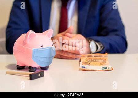 Nahaufnahme von Sparschwein, Tragen einer schützenden Gesichtsmaske. Sparkonzept zur Zeit der Coronavirus-Pandemie. Fünfzig Euro und Geschäftsmann im Hintergrund Stockfoto