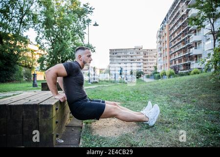 Ein kleiner kaukasischer Junge führt verschiedene Muskeltraining und Dehnung durch Übungen im Freien in einem Park Training Bizeps und Trizeps Stockfoto