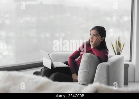 Allein mit dem Laptop von zu Hause aus gelangweilt zu arbeiten. Procrastination, müde asiatische junge Frau, Remote-Arbeit online am Computer im Wohnzimmer zu tun. Einengung Stockfoto