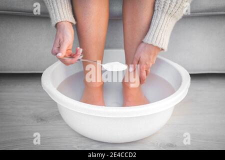 Frau legte Löffel Backpulver in Bad mit heißem Wasser für ihre Füße. Hausgemachtes Bad für trockene Füße Haut. Stockfoto