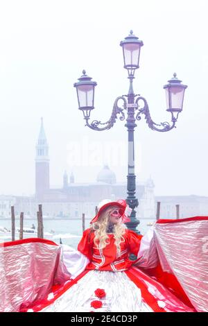 Italien, Venetien, Venedig, Frau im roten Kleid Kostüm beim karneval in venedig, nebliger Morgen in der venezianischen Lagune Stockfoto