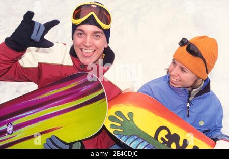 Zwei Teenager halten mit ihren farbenfrohen Snowboards für ein informelles Portrait vor einer Schneebank im Whitefish Mountain Resort in Whitefish, Montana, USA. Das Snowboarden wurde in den 1960er Jahren in den Vereinigten Staaten entwickelt und kombiniert die Elemente Skifahren, Skateboarden und Surfen. Als seine Popularität wuchs bundesweit in den nächsten zwei Jahrzehnten, einige Skigebiete zunächst verboten den Sport auf ihren Pisten. Alle vier Jahre seit 1998 bekommt das Snowboarden bei den Olympischen Winterspielen internationale Aufmerksamkeit. Stockfoto