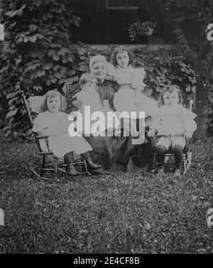 Amerikanisches Archiv monochromes Familienportrait in einem Garten mit einer Großmutter und vier kleinen Enkeln zwei Kinder sitzen in Schaukelstühlen und zwei Kinder sitzen auf dem Schoß ihrer Großmutter. Aufgenommen im späten 19. Jahrhundert in Port Byron, NY, USA Stockfoto