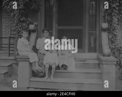 Amerikanisches Archiv monochromes Familienportrait einer Mutter und drei Kindern, die auf Stufen vor einem Backsteinhaus sitzen. Datiert Sommer 1894. Aufgenommen im späten 19. Jahrhundert in Port Byron, New York, USA Stockfoto