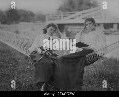 Amerikanisches Archiv monochromes Porträt von zwei Mädchen oder jungen Frauen in einer Gartenhängematte. Eine junge Frau hält einen Blumenstrauß und die andere Frau hält ein Buch. Aufgenommen im späten 19. Jahrhundert in Port Byron, NY, USA Stockfoto