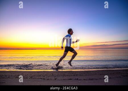 Man 50 plus fit, Sport bei Sonnenaufgang am Meer. Laufen am Strand von Scharbeutz. Stockfoto