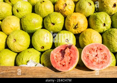 Zwei Hälften von roten und hellgrünen nassen Gavas öffneten sich Mit einem Obststapel dahinter Stockfoto