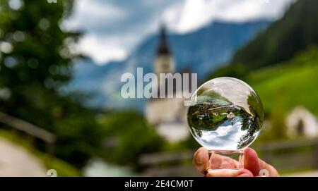 Blick durch Glaskugel zur Pfarrkirche St. Sebastian, Ramsauer Ache, hinten Reiteralpe, Ramsau, Berchtesgaden, Berchtesgadener Land, Oberbayern, Bayern, Deutschland, Europa Stockfoto