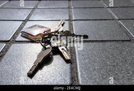 Ein verlorener oder fallengegangener Schlüsselanhänger mit mehreren Schlüsseln, die an ihm befestigt sind, auf einem gefliesten Steinboden. Stockfoto