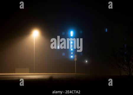 Nebel in den Straßen der Stadt Luckenwalde, beleuchtete Fenster im Hintergrund, im Vordergrund eine Straßenlaterne Stockfoto