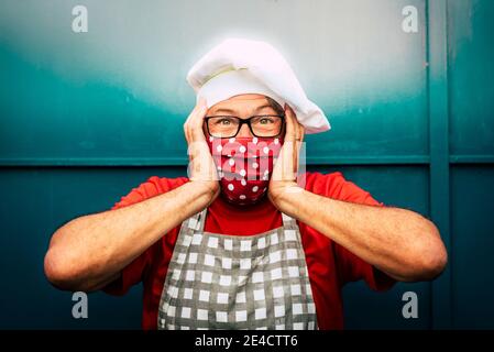 Portrait von fröhlichen und verwüsteten erwachsenen Mann mit toque und Gesichtsmaske für Coronavirus covid-19 Virus Notfall - Konzept der weihnachten und Feiertage allein während der Sperre Stockfoto