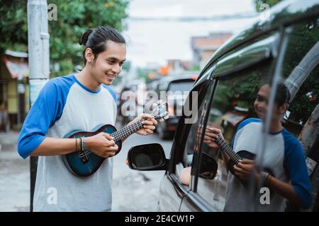 Busker benutzen Musikinstrumente und singen neben einem geparkten Auto Am Straßenrand Stockfoto