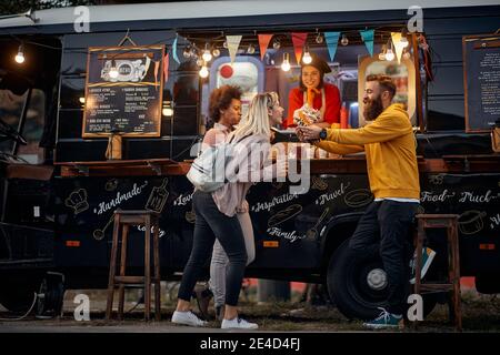 Gruppe von multiethnischen jungen Menschen Spaß beim Essen in Vorderseite des modifizierten LKW für mobilen Fast-Food-Service Stockfoto