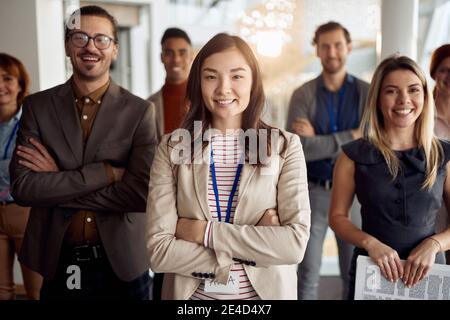Junge asiatische Geschäftsfrau, vor ihrem Team stehen. Arme gekreuzt, lächelnd, Blick auf die Kamera. Blickkontakt Stockfoto
