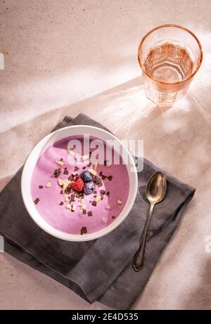 Ein einfaches Sommeressen aus einer großen Schüssel Beeren Joghurt mit etwas Schokolade und Nüsse als Belag und Ein Glas Wasser Stockfoto