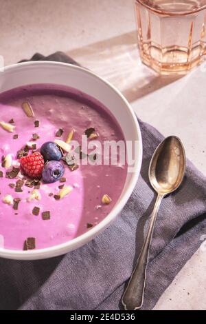 Nahaufnahme eines lila Beeren Joghurt mit einigen Heidelbeeren, Himbeeren, Mandel und Schokolade Chips auf der Oberseite Stockfoto