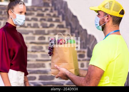 Lieferung kaukasischen Mann Lebensmittelgeschäft Lieferung Kurier Mann in gelber Uniform und Gesichtsmaske mit kleinen Box mit frischem Obst und Gemüse. Essen und Lieferung Stockfoto