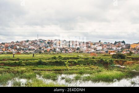 Antananarivo, Madagaskar - 24. April 2019: Typische Landschaft während des bewölkten Tages in der Nähe von Madagaskar Hauptstadt, Häuser auf kleinen Hügeln Hintergrund, mit Menschen Stockfoto