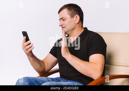 Profilfoto. Ein älterer Mann winkt bei einem Videoanruf mit der Hand in ein Grußzeichen und kommuniziert mit nonverbalen Gesten. Weißer Hintergrund. Stockfoto