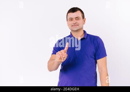 Der Kaukasusmann zeigt seinen Zeigefinger nach oben. Schwerhöriger Mann im lässigen T-Shirt auf weißem Hintergrund mit leerem Seitenraum. Stockfoto