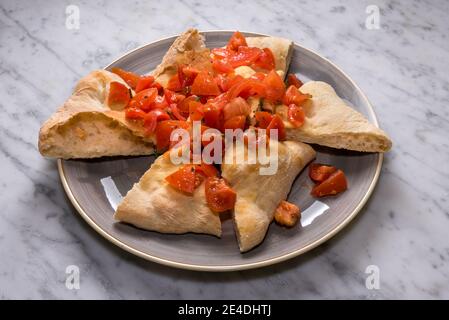 Focaccia Brotscheiben mit rohen gehackten Kirschtomaten, Gewürzen und Olivenöl in grauer Schale auf Marmoroberfläche Stockfoto