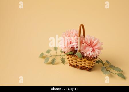 Minimales Konzept einer kleinen Bouqet aus rosa Blüten und Blättern im Weidenkorb. Vintage Frühjahrskonzept. Beigefarbener Hintergrund in Pastelltönen Retro-Mode aest Stockfoto