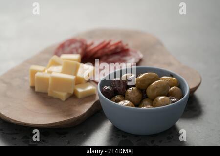 Oliven, Salami und Jahrgangskäse auf Betonarbeitsplatte, flacher Fokus Stockfoto