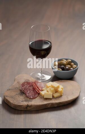 Oliven, Salami und Jahrgangskäse mit einem Glas Rotwein auf Walnusstisch, flacher Fokus Stockfoto