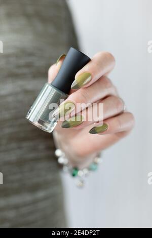 Frauenhand mit langen Nägeln und hellgrüner Maniküre mit Nagellackflaschen. Stockfoto