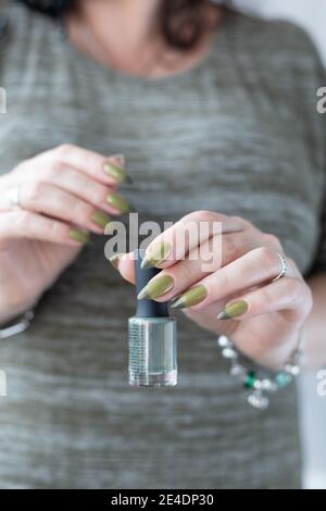 Frauenhand mit langen Nägeln und hellgrüner Maniküre mit Nagellackflaschen. Stockfoto