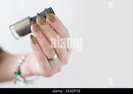 Frauenhand mit langen Nägeln und hellgrüner Maniküre mit Nagellackflaschen. Stockfoto