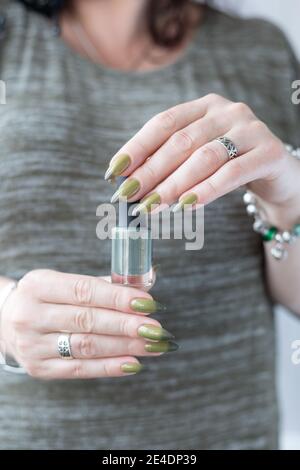 Frauenhand mit langen Nägeln und hellgrüner Maniküre mit Nagellackflaschen. Stockfoto