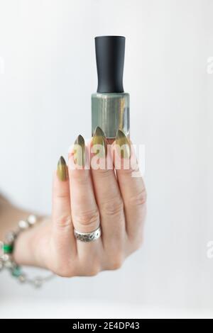 Frauenhand mit langen Nägeln und hellgrüner Maniküre mit Nagellackflaschen. Stockfoto