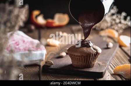 Köstliche frische hausgemachte Muffins wird mit Schokolade auf einem Holztisch gegossen. Stockfoto