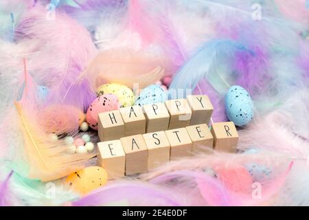 Frohe Ostern geschrieben mit Holzwürfeln umgeben von schönen pastellfarbenen dekorativen Federn und Eiern, April, Ostern, Religion, Frühlingskonzept Stockfoto