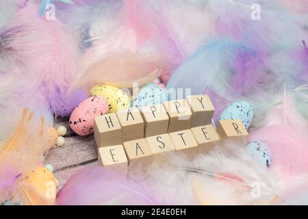 Frohe Ostern geschrieben mit Holzwürfeln umgeben von schönen pastellfarbenen dekorativen Federn und Eiern, April, Ostern, Religion, Frühlingskonzept Stockfoto