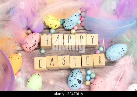 Frohe Ostern geschrieben mit Holzwürfeln umgeben von schönen pastellfarbenen dekorativen Federn und Eiern, April, Ostern, Religion, Frühlingskonzept Stockfoto