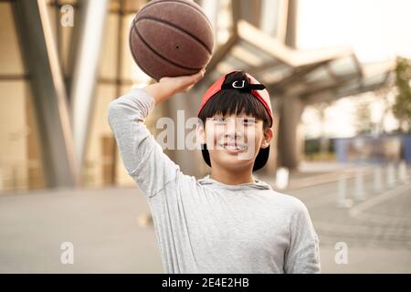 Outdoor-Porträt eines glücklichen fünfzehnjährigen asiatischen Teenager-Basketballspieler Stockfoto
