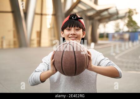 Outdoor-Porträt eines glücklichen fünfzehnjährigen asiatischen Teenager-Basketballspieler Stockfoto